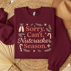 Pu&ograve; includere: Felpa bordeaux con la scritta "Sorry. Can't. Nutcracker Season." in un design festivo. Presenta scarpette da ballo, bastoncini di zucchero e fiocchi di neve. Un capo d'abbigliamento stagionale e accogliente.