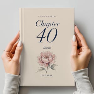 Peut inclure: Un livre crème avec le texte "A New Chapter" et "Chapter 40" en bleu marine. En dessous, le nom "Sarah" et une illustration de pivoine à l'aquarelle. Le bas du livre indique "EST 1986".