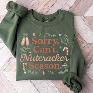 Pu&ograve; includere: Felpa verde con la scritta "Sorry. Can't. Nutcracker Season." in un design festivo. Il design include scarpette da ballo, bastoncini di zucchero e fiocchi di neve. Le maniche sono arricciate.