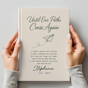 May include: A cream-colored journal with the text "Until Our Paths Cross Again" and a paper airplane illustration. The journal includes a personalized message and the name "Stephanie" with the year "EST. 2019".