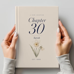 May include: A cream-coloured book cover with the text "A New Chapter" and "Chapter 30" in navy blue. The name "Sarah" is below the chapter number, and a watercolour daffodil illustration is at the bottom. The text "EST. 1986" is also visible.