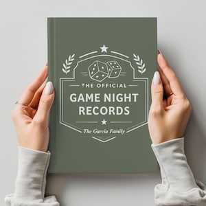 May include: A sage green notebook with the text "THE OFFICIAL GAME NIGHT RECORDS" in white. The design includes dice, stars, and laurel leaves. The family name "The Garcia Family" is also displayed.