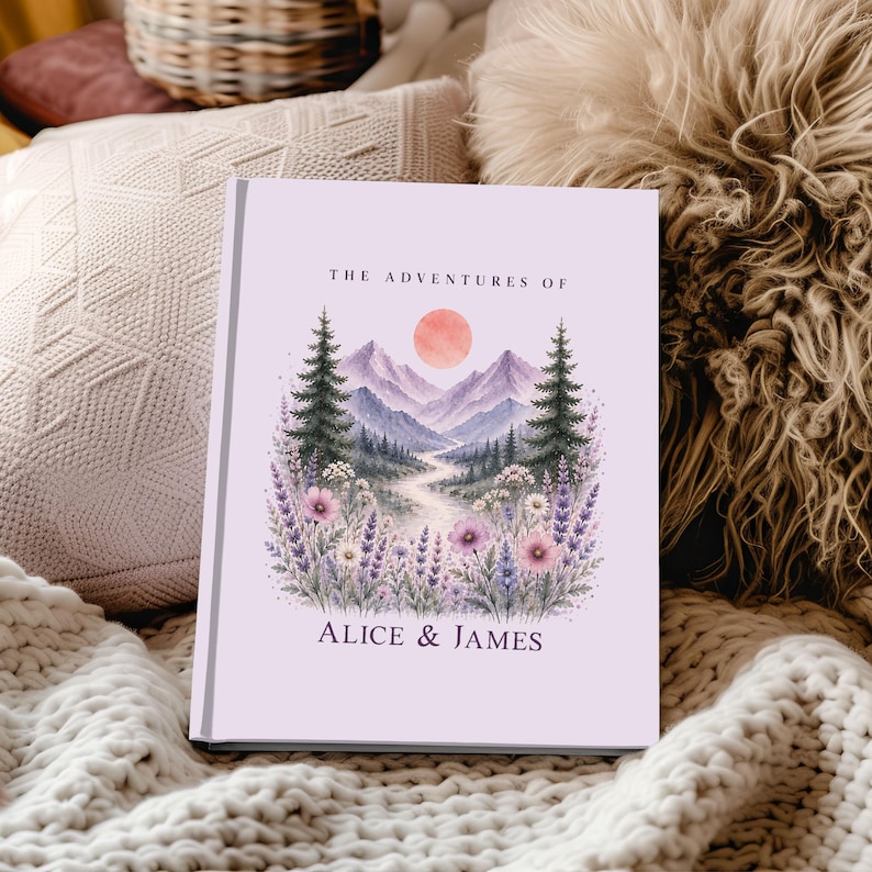 May include: A hardcover book with a light purple cover featuring a watercolor landscape. The illustration includes mountains, trees, a setting sun, and a path. The text "THE ADVENTURES OF" and "ALICE & JAMES" are visible.
