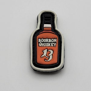 Może przedstawiać: Czarno-biała łatka z białym obramowaniem. Łatka przedstawia kreskówkową ilustrację butelki bourbona z napisem "Bourbon Whiskey" i numerem "13" na etykiecie.