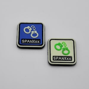May include: Two white and black iron-on patches with a handcuff design. The patch on the left is blue with white handcuffs and the text "SPANXXX". The patch on the right is white with green handcuffs and the text "SPANXXX".