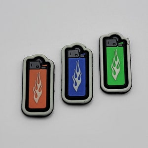 May include: Three iron-on patches featuring a lighter with a flame design. The patches are in orange, blue, and green.