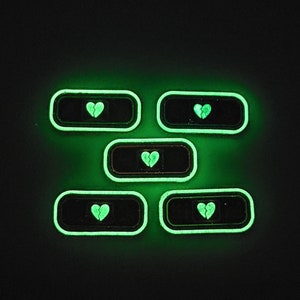 May include: Five glow-in-the-dark green adhesive bandages with a broken heart design.