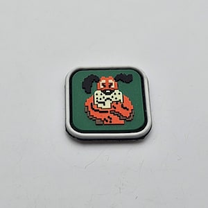 Pode incluir: Um remendo quadrado branco com uma borda verde e uma imagem pixelada de um cão de sangue vermelho e branco. O cão está usando uma coleira branca com uma gravata borboleta preta.