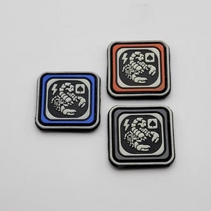 Könnte beinhalten: Drei gestickte Patches mit einem Skorpion-Motiv. Die Patches sind in blauen, orangen und schwarzen Rahmen. Jeder Patch hat einen Blitz und ein Pik-Symbol.
