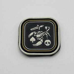 May include: A white scorpion with a spade and skull design on a black background. The patch is surrounded by a yellow border and a white outer border.