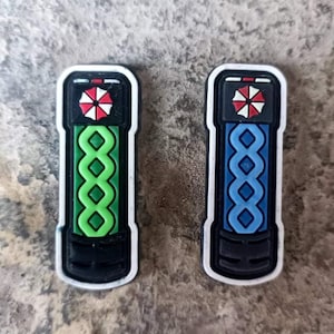 May include: Two black and white patches with a green and blue design. The patches feature a white umbrella with a red circle in the center. The patches are approximately 2 inches tall.