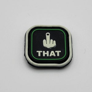 May include: Black and green patch with a white middle finger and the word "THAT" in white letters.