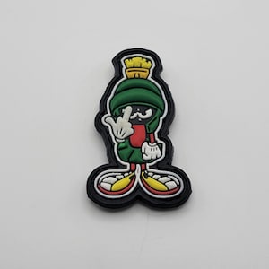 Może przedstawiać: Czarno-zielona postać z kreskówki z żółtym pędzlem na głowie, pokazująca środkowy palec. Postać ma na sobie czerwono-białe buty.