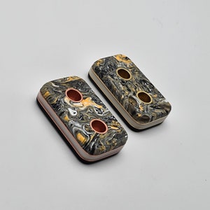 May include: Two black and gold marbled rectangular buttons with two holes each. The buttons have a white border and a copper trim.