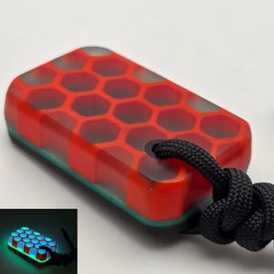 May include: A rectangular fidget toy with a red honeycomb design over a translucent material. The edges are green and the toy has a black cord attached. A smaller, glowing version of the toy is in the corner.
