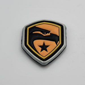 Peut inclure: Un patch thermocollant noir et jaune avec une tête d'aigle stylisée et une étoile à l'intérieur d'un bouclier.