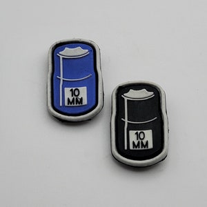 May include: Two white plastic patches with black outlines. Each patch features a black and white illustration of a barrel with the text "10 MM" printed on it. One barrel is blue and the other is black.