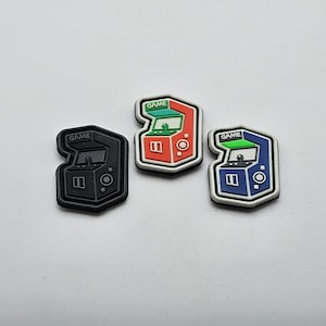 Könnte beinhalten: Drei Bügelbilder mit Retro-Arcade-Spielautomaten. Die Patches sind schwarz, rot und blau mit dem Wort "GAME" auf jedem.
