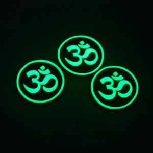 May include: Three glow-in-the-dark round stickers with the Om symbol in green on a black background.