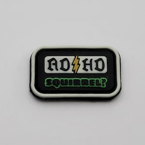 May include: Black and white patch with a white border. The patch has the text "ADHD" in black with a yellow lightning bolt in between the letters. Below the text is the text "SQUIRREL?" in green.