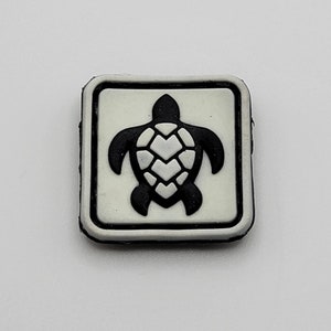 Könnte beinhalten: Ein weißer quadratischer Patch mit schwarzem Rand und einer schwarzen Silhouette einer Meeresschildkröte mit weißer Schale.