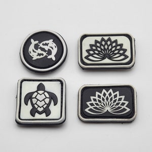 May include: Four black and white embroidered patches with different designs. The designs include a lotus flower, a turtle, and two fish.