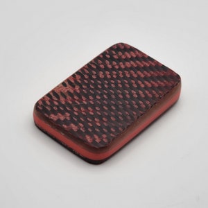 Puede incluir: Una baldosa rectangular de color rojo oscuro y negro con un fino borde rojo.