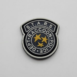 Puede incluir: Un parche bordado en blanco y negro con el texto "S.T.A.R.S. Raccoon City Police Dept." y tres estrellas amarillas.
