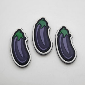 May include: Three purple eggplant shaped patches with green tops. The patches are outlined in white and have a white background.