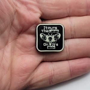 May include: A black and white square patch with a moth and the text "It puts the lotion on its skin".