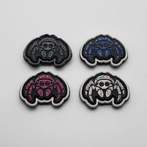 Könnte beinhalten: Vier Bügelbilder mit einem Spinnen-Design mit bunten Streuseln. Die Spinnen sind in Schwarz, Weiß, Blau und Pink.