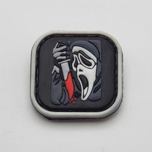 May include: A black and white patch with a white ghost figure holding a red knife. The ghost is wearing a black hooded robe and has a white mask with a scream face. The patch is surrounded by a white border.