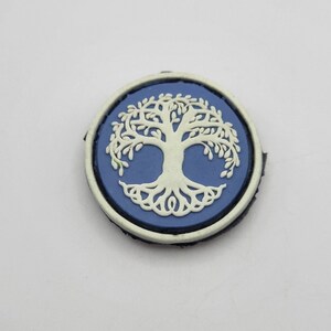 Peut inclure: Un patch rond bleu et blanc avec un motif d'arbre de vie. L'arbre est blanc avec un fond bleu et un contour blanc.