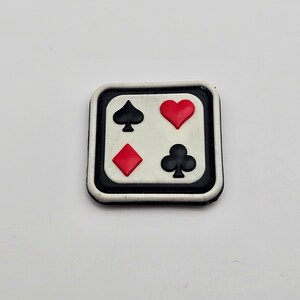 Puede incluir: Un dije cuadrado de carta de juego en blanco y negro, con los cuatro palos: picas, corazones, diamantes y tréboles. Los palos son rojos y negros sobre un fondo blanco, con un borde negro y un borde exterior blanco.