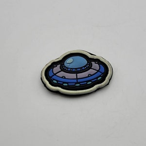 May include: A white, blue, and purple cartoon UFO patch with a black outline.
