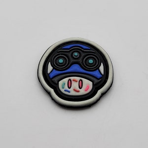 May include: A black and white cartoon character with blue eyes and a blue hat. The character has a white face with pink and blue sprinkles.