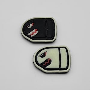 May include: Two black and white bullet-shaped patches with a cartoon character's face on each. The character has a single eye and a jagged mouth.