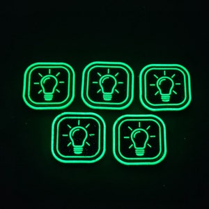 May include: Six green glow-in-the-dark square stickers with a light bulb icon inside each.