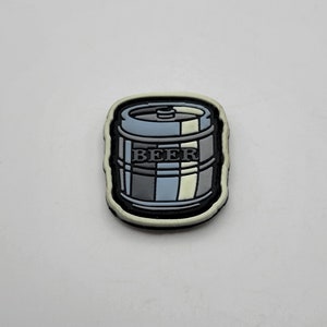May include: A black and white patch with a cartoon image of a beer keg. The keg is gray and white with the word "BEER" printed on it.