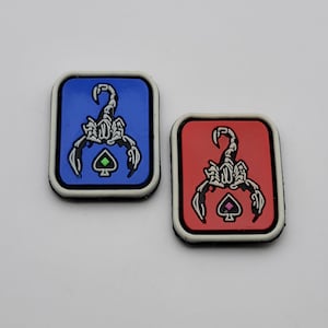 Könnte beinhalten: Zwei rechteckige Aufnäher mit einem Skorpion-Design. Einer ist blau mit einem weißen und schwarzen Skorpion und einem grünen Pik. Der andere ist rot mit einem weißen und schwarzen Skorpion und einem rosa Pik.