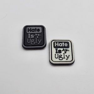 May include: Two square patches with the text "Hate Is Ugly" in black and white. The patches are made of a rubber-like material and have a textured surface.