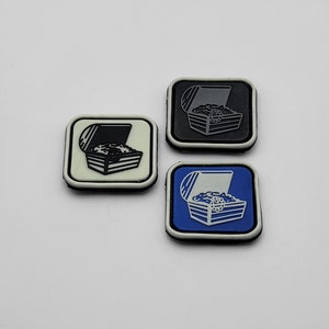 Può includere: Tre toppe ricamate con un design a forma di forziere. Le toppe sono nere, bianche e blu. Il forziere è pieno di monete d'oro.