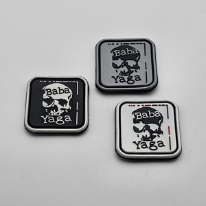 Puede incluir: Tres parches bordados en blanco y negro con un diseño de calavera y huesos cruzados. Los parches tienen el texto "Baba Yaga".