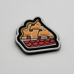 May include: A white, black, and red rubber patch with a cartoon image of a pie. The pie has a yellow and orange filling and a red crust.