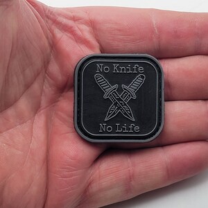 Pu&ograve; includere: Toppa quadrata nera con contorno bianco e il testo "No Knife No Life" in bianco. Due coltelli incrociati sono raffigurati al centro della toppa.