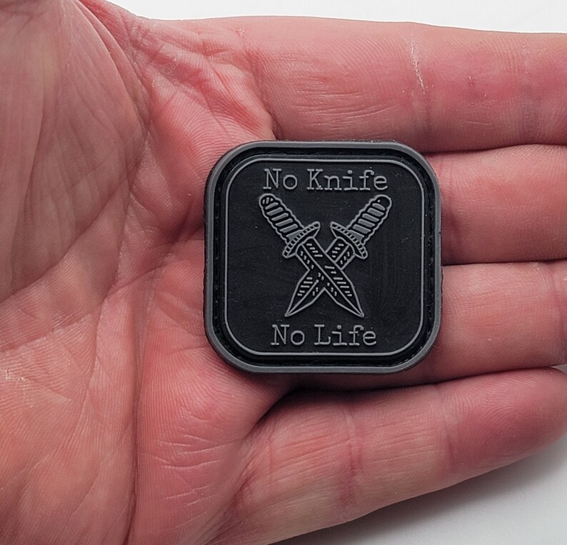 Pu&ograve; includere: Toppa quadrata nera con contorno bianco e il testo "No Knife No Life" in bianco. Due coltelli incrociati sono raffigurati al centro della toppa.