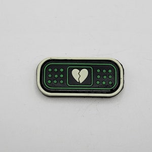 May include: Black and white band-aid patch with a green border and a broken heart design.