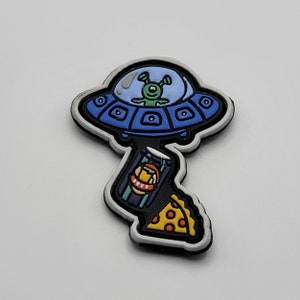 Puede incluir: Una nave espacial extraterrestre azul y blanca con un extraterrestre verde en su interior, una lata de cerveza y una rebanada de pizza. La imagen es un parche o una pegatina.