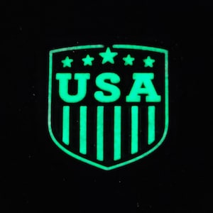 May include: A green glow-in-the-dark shield-shaped patch with the word "USA" and five stars at the top.