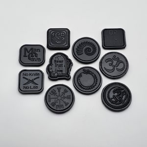 May include: Ten black round and square patches with various designs, including a scorpion, a nautilus shell, a tombstone with the text "Never Trust the Living", a compass, an alien, an Om symbol, a snake, and the text "Man Cave" and "No Knife No Life".